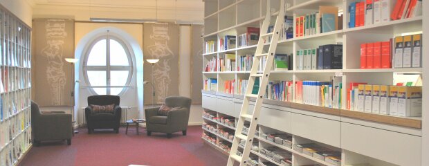 vorderer Teil der Bibliothek des Studienortes Fürstenfeldbruck, auf der linken Seite befindet sich das Zeitschriftenregal, in der Mitte die Sesselecke, auf der rechten Seite das erste der großen Bücherregale. Bibliothek des Studienortes Fürstenfeldbruck
