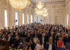 Festgäste sitzen im Max-Joseph-Saal, dessen Wände und Decken verzierte Stuckarbeiten schmücken, während imposante Kronleuchter warmes Licht spenden.